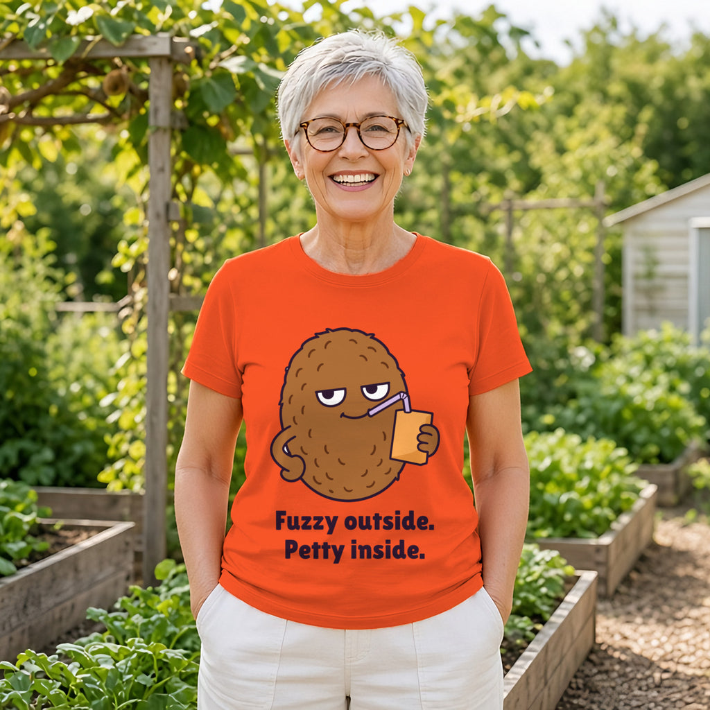 Woman with a silver pixie cut and glasses wearing the orange Petty Kiwi tee in a garden
