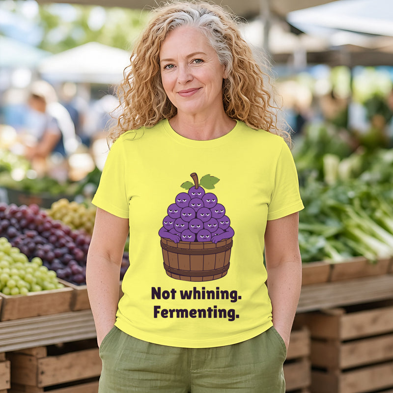 Woman with curly strawberry-blonde hair wearing the cornsilk yellow Grumpy Grapes tee at a produce market