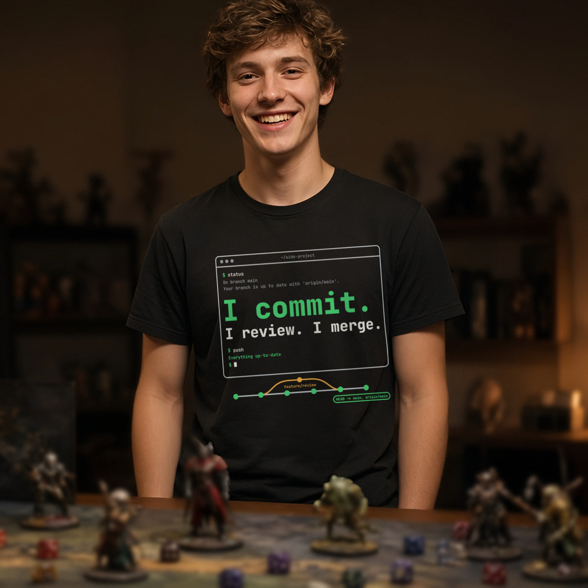 Man wearing a black t-shirt printed with 'I commit. I review. I merge.' (clean version), at a tabletop RPG table. Model image is digitally generated. The print shown is the actual design; colours and fit may vary slightly, see size chart.