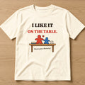 Natural t-shirt, flat lay, printed with 'I like it on the table. (Board games. Obviously.)'
