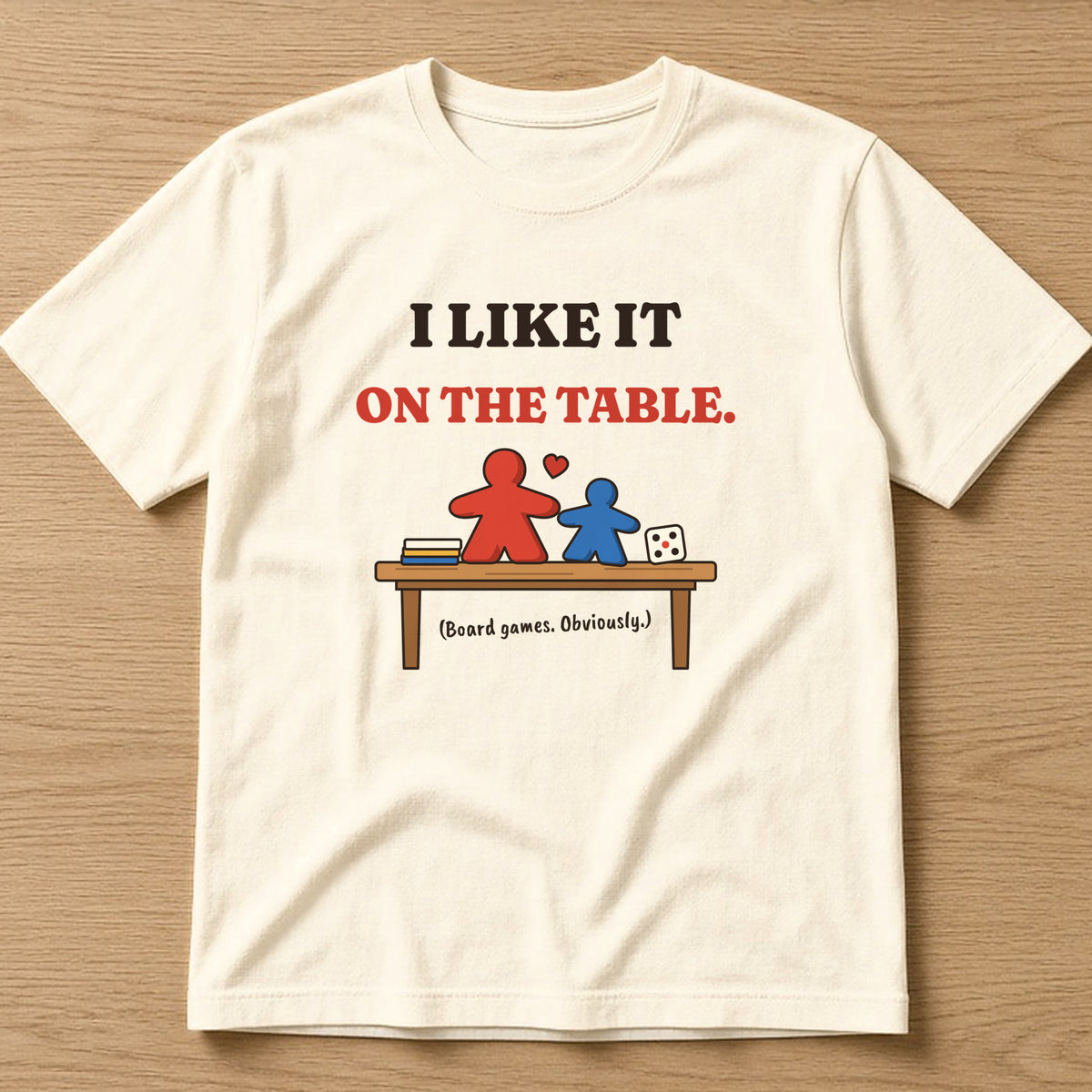 Natural t-shirt, flat lay, printed with 'I like it on the table. (Board games. Obviously.)'
