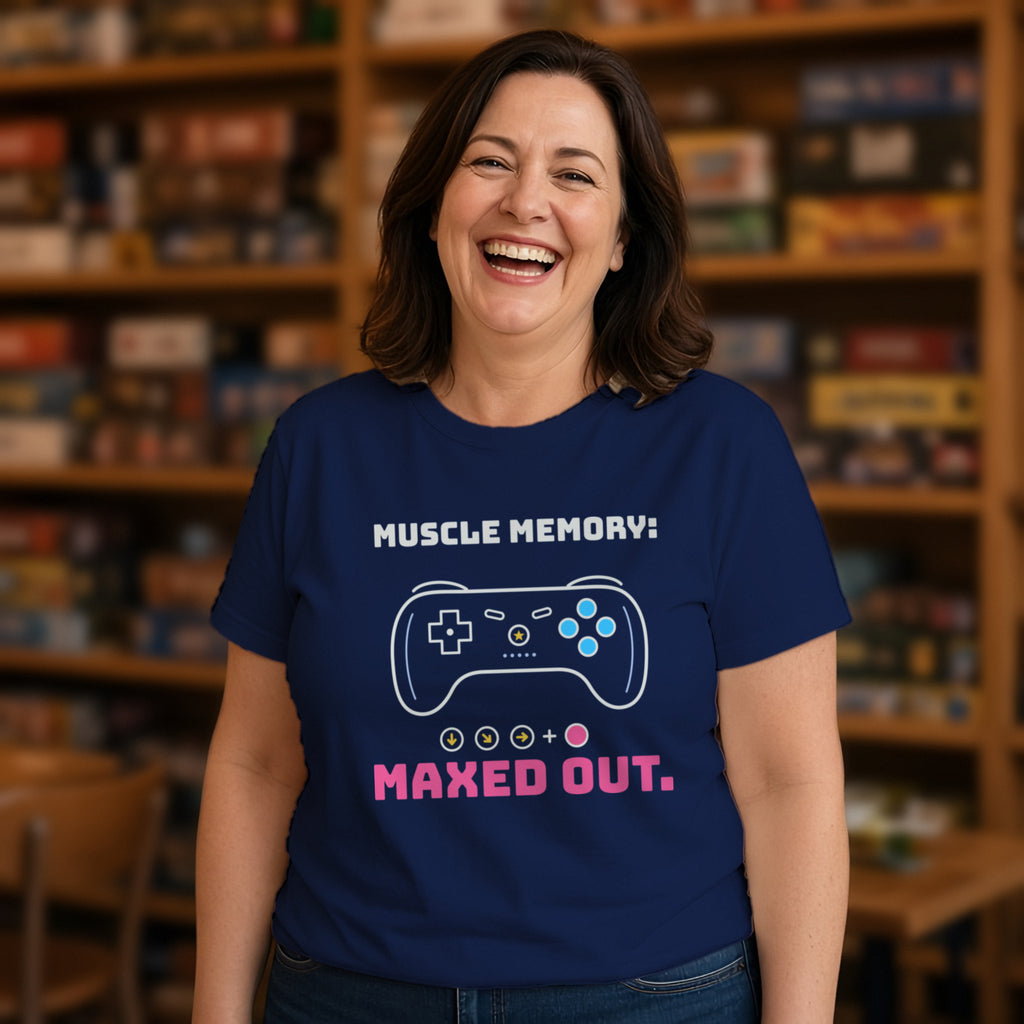 Woman wearing a navy t-shirt printed with 'Muscle memory: maxed out.' (clean version), in a board game cafe. Colours and fit may vary slightly, see size chart.