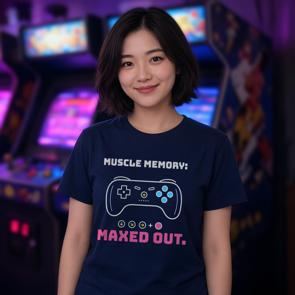 Woman wearing a navy t-shirt printed with 'Muscle memory: maxed out.' (clean version), in an arcade. Colours and fit may vary slightly, see size chart.