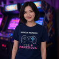 Woman wearing a navy t-shirt printed with 'Muscle memory: maxed out.' (clean version), in an arcade. Colours and fit may vary slightly, see size chart.