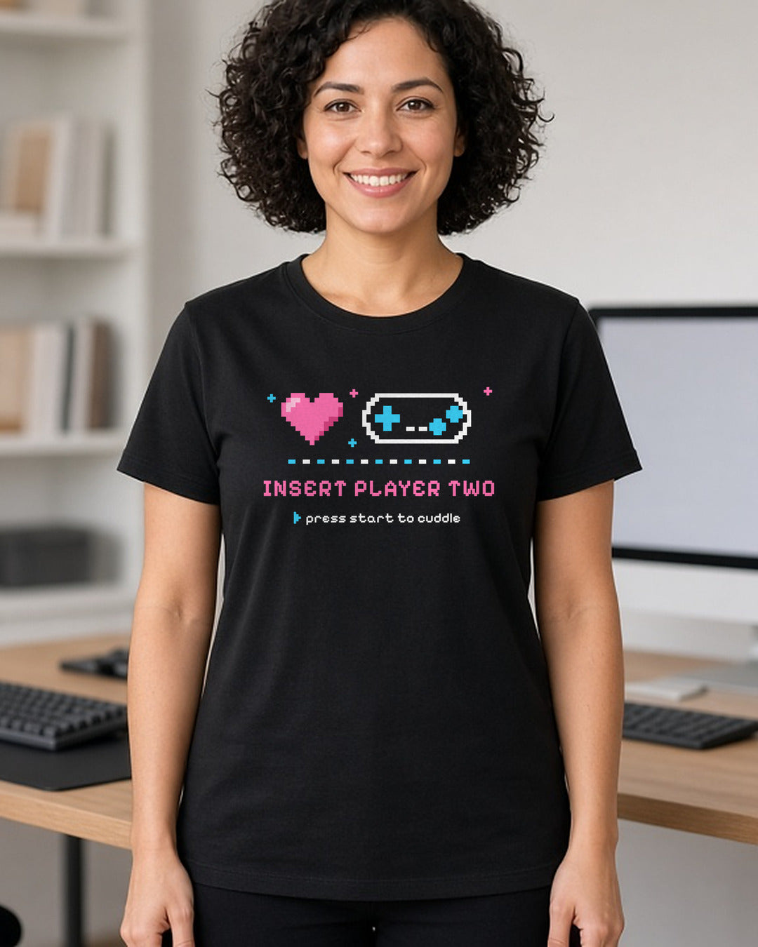Woman wearing a black t-shirt printed with 'Insert Player Two / press start to cuddle' (spicy version) (4:5 crop). Model image is digitally generated. The print shown is the actual design; colours and fit may vary slightly, see size chart.