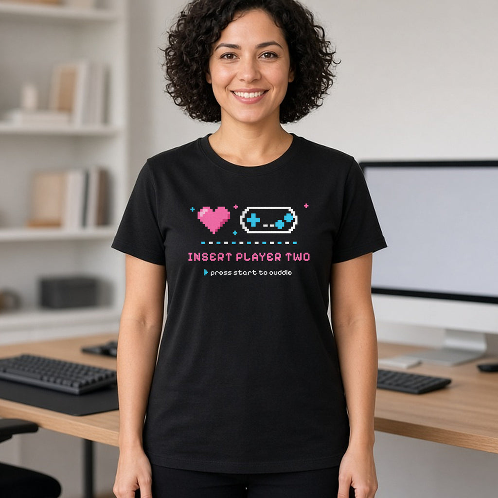 Woman wearing a black t-shirt printed with 'Insert Player Two / press start to cuddle' (spicy version). Model image is digitally generated. The print shown is the actual design; colours and fit may vary slightly, see size chart.